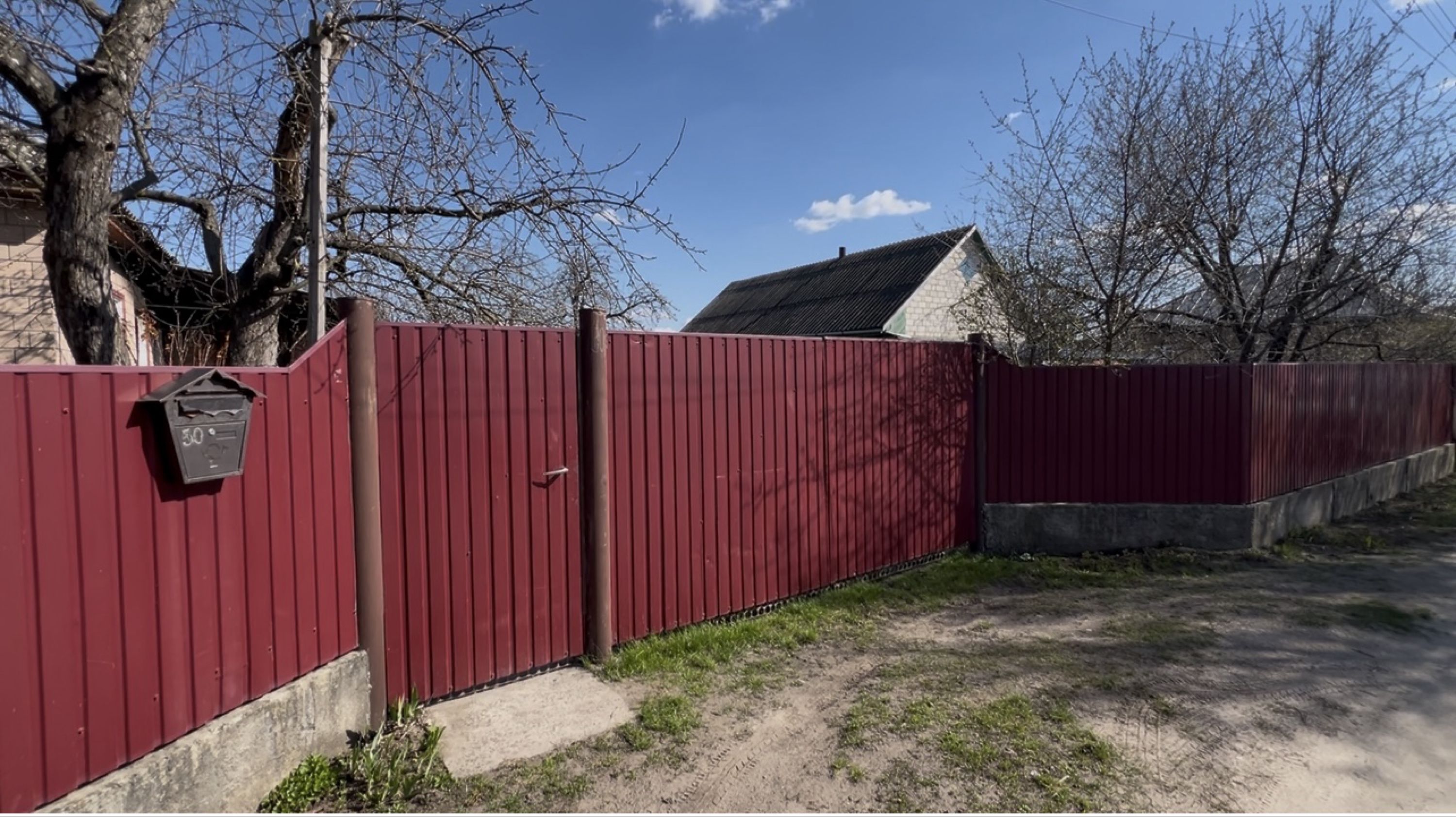Металевий паркан червоного кольору з хвірткою та поштовою скринькою біля входу.